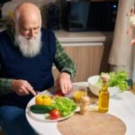 adulto mayor en la mesa de la cocina corta verduras y vegetales prohibidos para ensalada. Descubre como comerlos e incluirlos en la dieta, sus beneficios y contraindicaciones.